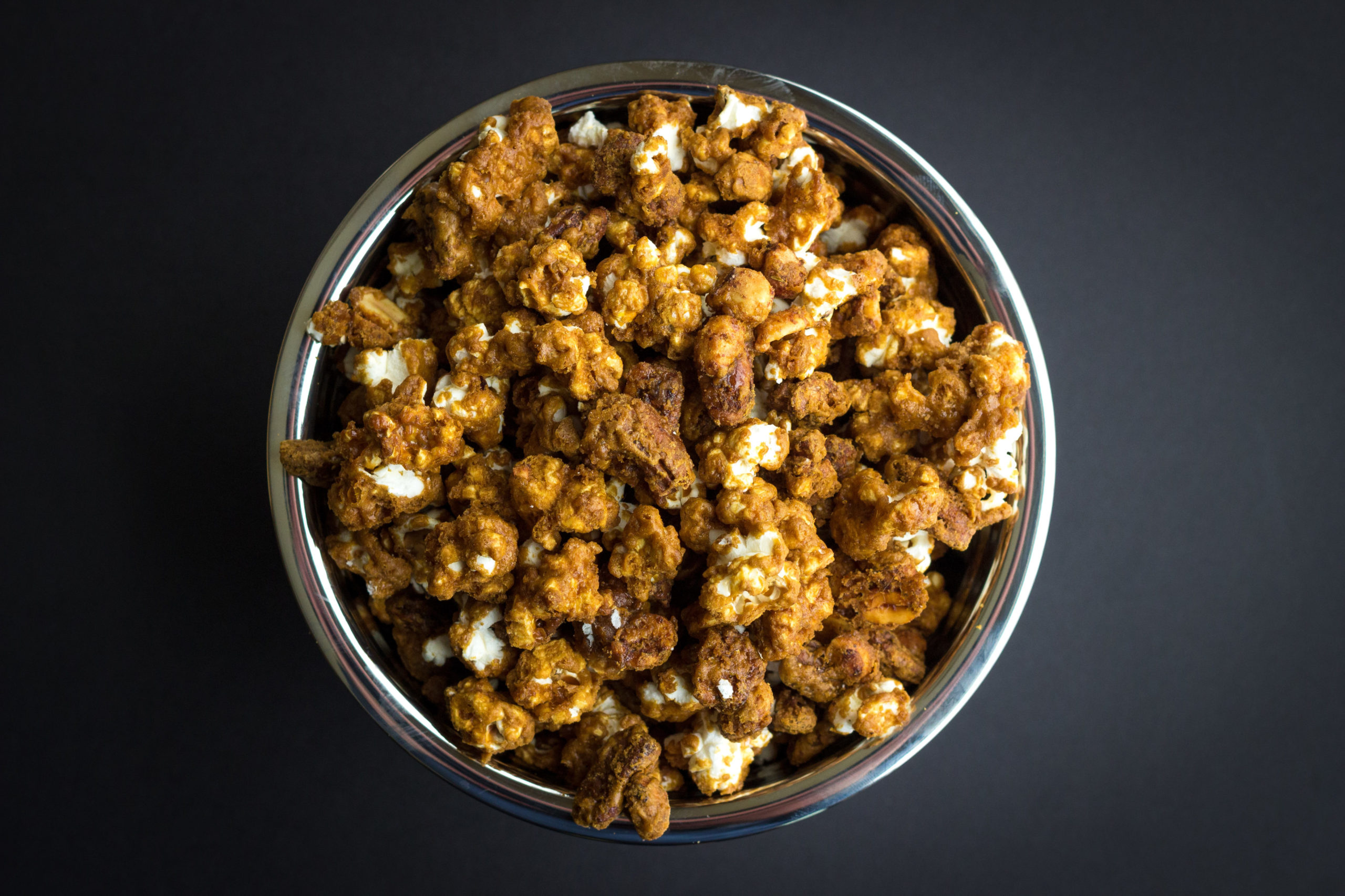 Overhead shot of silver bowl full of Cracker Jacks Remix on a black background